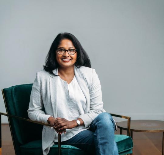 A woman with glasses sits in a green chair, appearing calm and engaged in her surroundings.