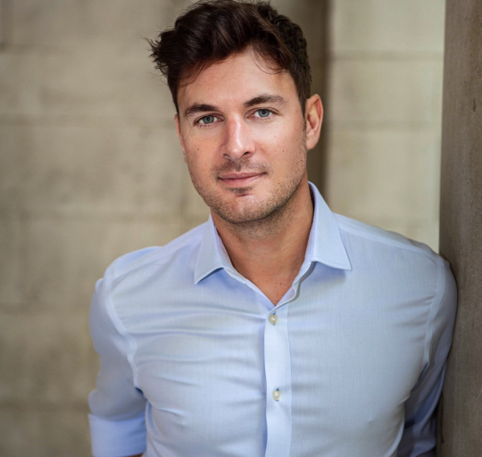  A man wearing a blue shirt stands against a wall,