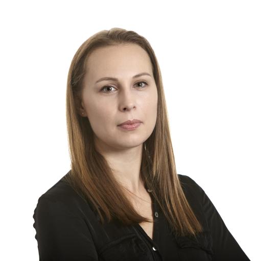 A woman with long hair wearing a black shirt, standing against a neutral background.