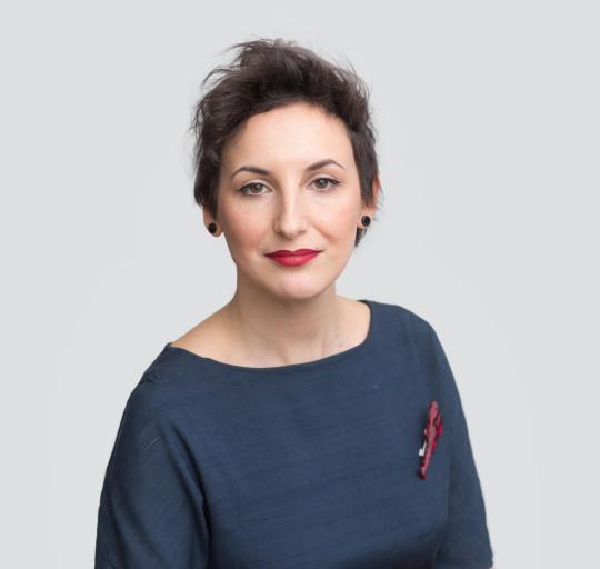 A professional portrait of a woman with short, dark hair styled in a textured cut. She is wearing a 