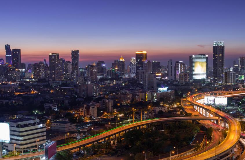 A city skyline at night with tall skyscrapers illuminated against a dark sky, reflecting on the water of a nearby lake or river. The scene captures the essence of a bustling metropolis with bright lights and urban architecture.